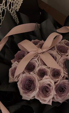 a bouquet of roses is wrapped in black paper and tied with a pink ribbon around it