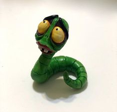 a green toy snake with yellow eyes on it's head and mouth, sitting on a white surface