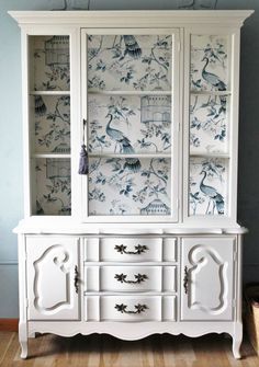 a white china cabinet with blue and white wallpaper