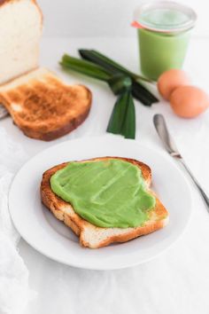 a white plate topped with a piece of bread covered in green spread next to eggs