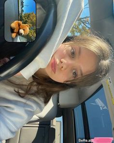 a woman sitting in the driver's seat of a car with a stuffed animal on her head