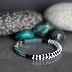 two bracelets with beads on them sitting next to some rocks and stones in the background