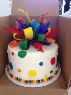 a birthday cake in a box decorated with multicolored ribbons and streamers on top