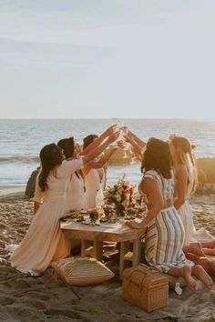 a group of women sitting on top of a sandy beach next to the ocean holding hands