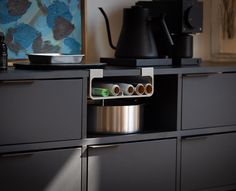 a coffee pot and some cups on top of a black cabinet in a living room