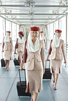 the women are walking with their luggage down the hall way in suits and headscarves