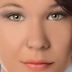 a woman's nose piercing is shown with green eyes and brown hair, while she has her nose ring in front of her face