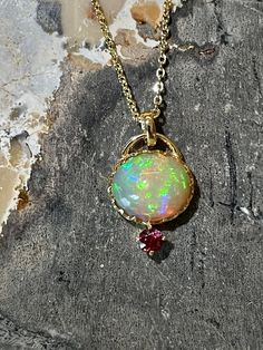 An amazing opal pendant with beautiful play of color! Set in a handmade 14k gold oval crown-style setting and adorned with a red spinel accent stone, this pendant is extremely elegant looking and mesmerising. Main Stone: natural untreated Opal Size: 11.3 x 9.4mm Weight: 3.75 carats Setting: 14k Solid Gold Accent Stone: Natural red spinel (3.5mm) Listing is for standalone pendant. Necklace can be purchased as an add-on option: - Add 925 Sterling Silver Gold Plated Necklace 30) - Add 14k solid gol Luxury Oval Opal Necklaces, Unique Oval 14k Gold Necklace, Elegant Ethiopian Opal Oval Cabochon Jewelry, Unique Oval Opal Necklaces, Oval Ethiopian Opal Necklace For Formal Occasions, Elegant Ethiopian Opal Cabochon Necklaces, Elegant Ethiopian Opal Oval Pendant Necklace, Handmade Oval Ethiopian Opal Necklaces, Handmade Oval Ethiopian Opal Necklace