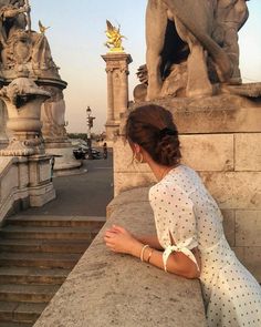 a woman sitting on top of a stone wall next to a stair case with statues in the background