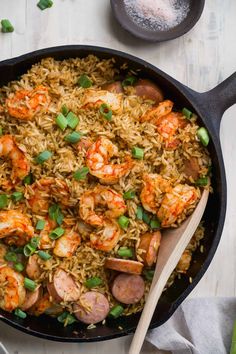 shrimp and rice in a skillet with a wooden spoon on the side next to it