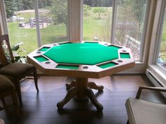 a pool table in the middle of a living room with large windows and chairs around it