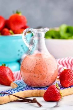 a glass pitcher filled with strawberry smoothie next to some strawberries on a table