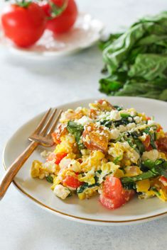 a white plate topped with an egg salad next to some spinach and tomatoes on a table