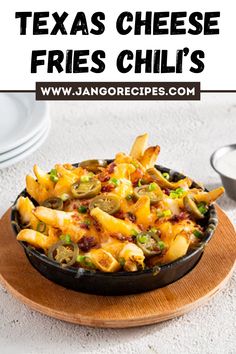 a skillet filled with cheesy fries on top of a wooden plate