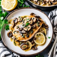 a white plate topped with chicken covered in mushrooms and lemon slices next to some silverware