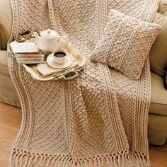 a crocheted blanket on a couch next to a cup and saucer