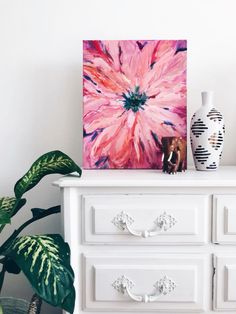 a white dresser topped with a pink flower painting