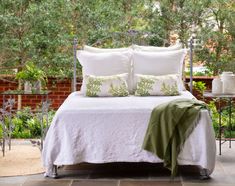 a bed with white linens and green pillows on top of it next to a brick wall