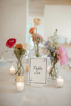 flowers and candles are sitting in vases on a table with a sign that says table six