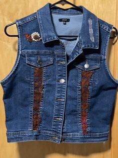 a denim vest with patches and buttons on the back, hanging on a wooden wall