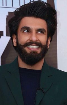 a man with a beard wearing a green suit and black shirt smiles at the camera