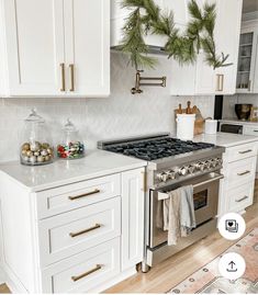 a kitchen with white cabinets and gold trim on the stove, christmas wreaths hanging above it