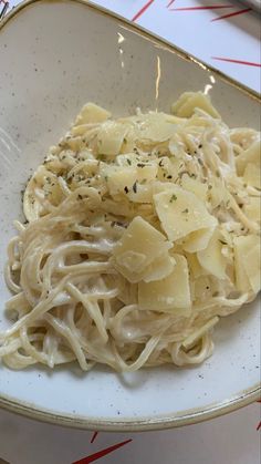 a white plate topped with pasta covered in parmesan cheese and seasoning next to a fork