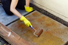 a person with yellow gloves is painting a concrete slab and holding a paint roller in their hand