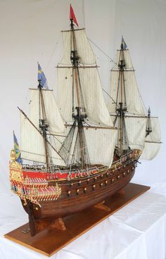 a model sailing ship on display on a wooden stand with white backdrop and red flag