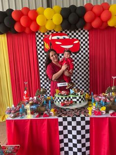 a woman holding a small child in front of a table with cake and balloons on it