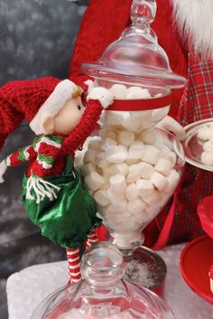 a glass jar filled with marshmallows on top of a table next to santa clause