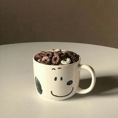 a white coffee cup filled with cereal and marshmallows sitting on top of a table