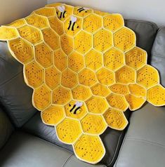 a yellow crocheted blanket sitting on top of a black leather couch next to a gray chair