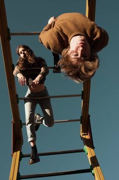 two people are hanging upside down on a ladder