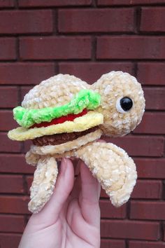 a hand holding a stuffed animal with a hamburger on it