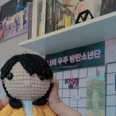 a crocheted doll is held up in front of a wall with posters on it