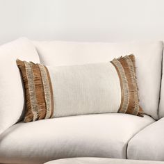 a white couch with brown and tan pillows on it's back end, next to a footstool