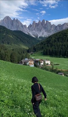 a woman walking through a lush green field with mountains in the backgrouund