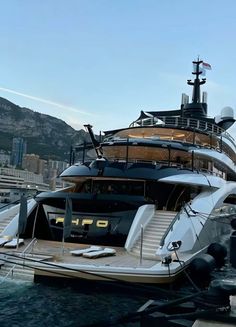 a large boat docked in the water near some buildings and boats on the water with mountains in the background