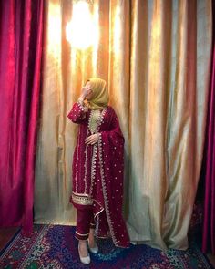 a woman standing in front of a curtain with her hands on her face and wearing a red outfit