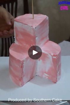 someone is decorating a cake with pink icing and a toothpick on top