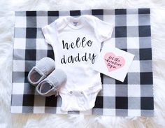 a baby's outfit and booties are laying on a plaid blanket with the words hello daddy written on it