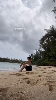 a man sitting on top of a sandy beach next to the ocean under a cloudy sky