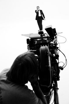 a black and white photo of a man in a suit standing on top of a camera