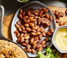 nuts and other food items on a cutting board next to a bowl with dip in it