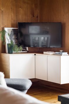 a flat screen tv sitting on top of a white cabinet in front of a wooden wall