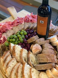 a platter with bread, grapes, meats and wine