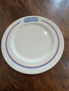 a white plate with blue and red lines on the rim sitting on a wooden table