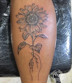 a woman's leg with a sunflower tattoo on it and a hand holding a flower