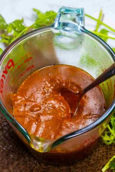 a glass measuring cup filled with sauce on top of a cloth covered table next to green plants